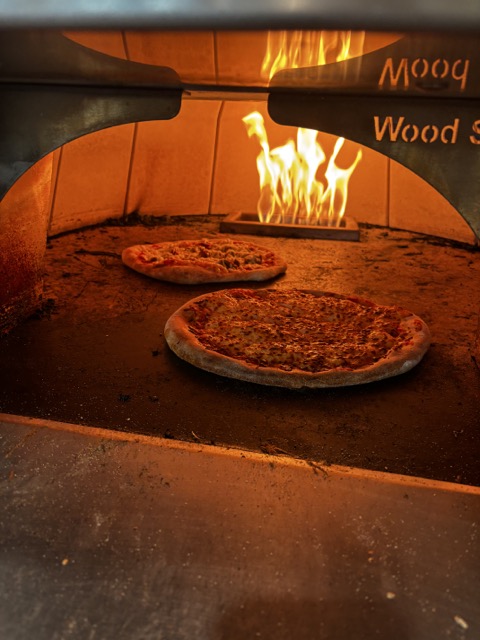 Finished pizza baking in wood-fired oven made with Forno Medici dough